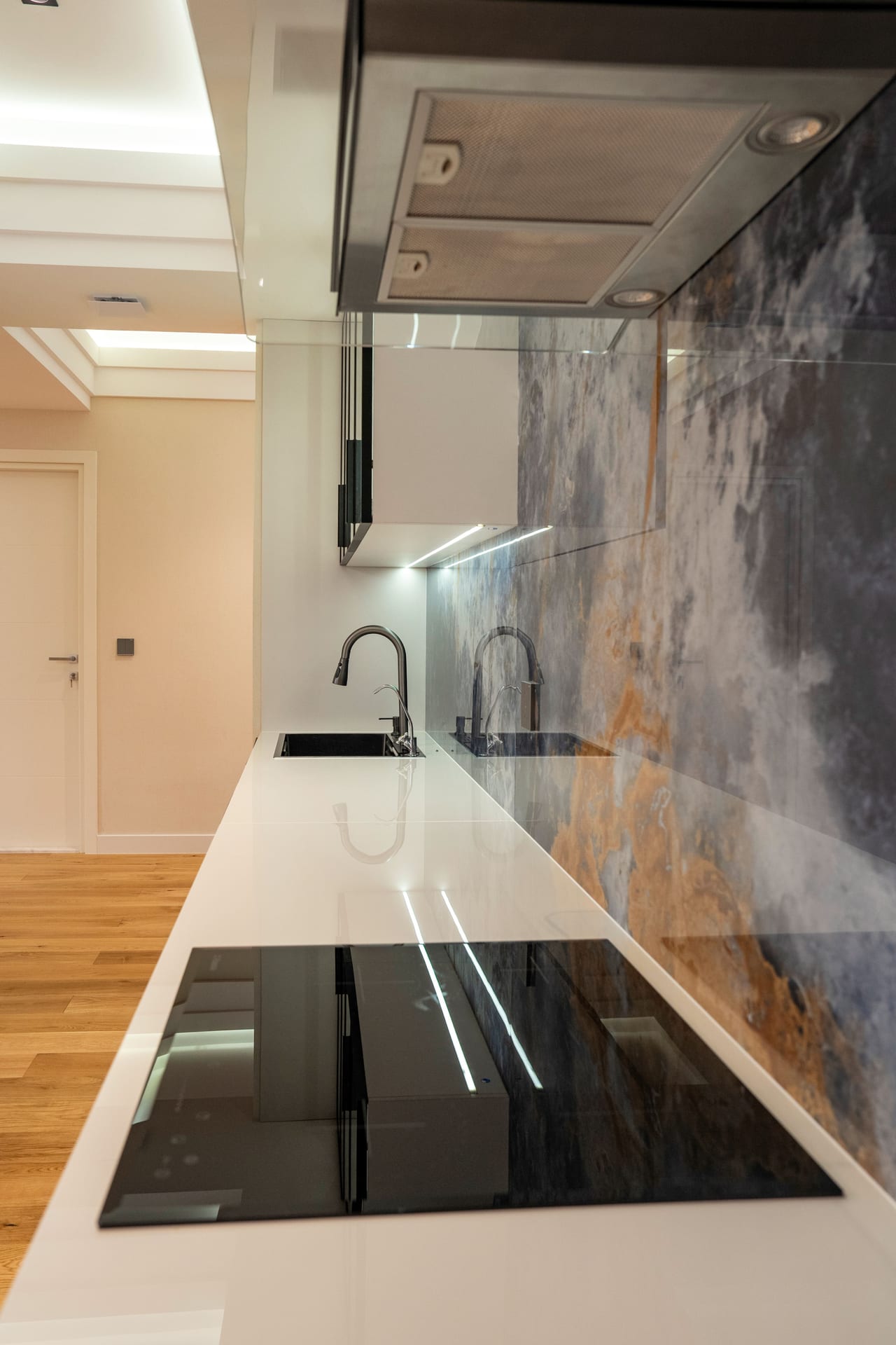 Projects Renovated modern kitchen with white island worktop, black cooktop and veined stone splashback in Alanya