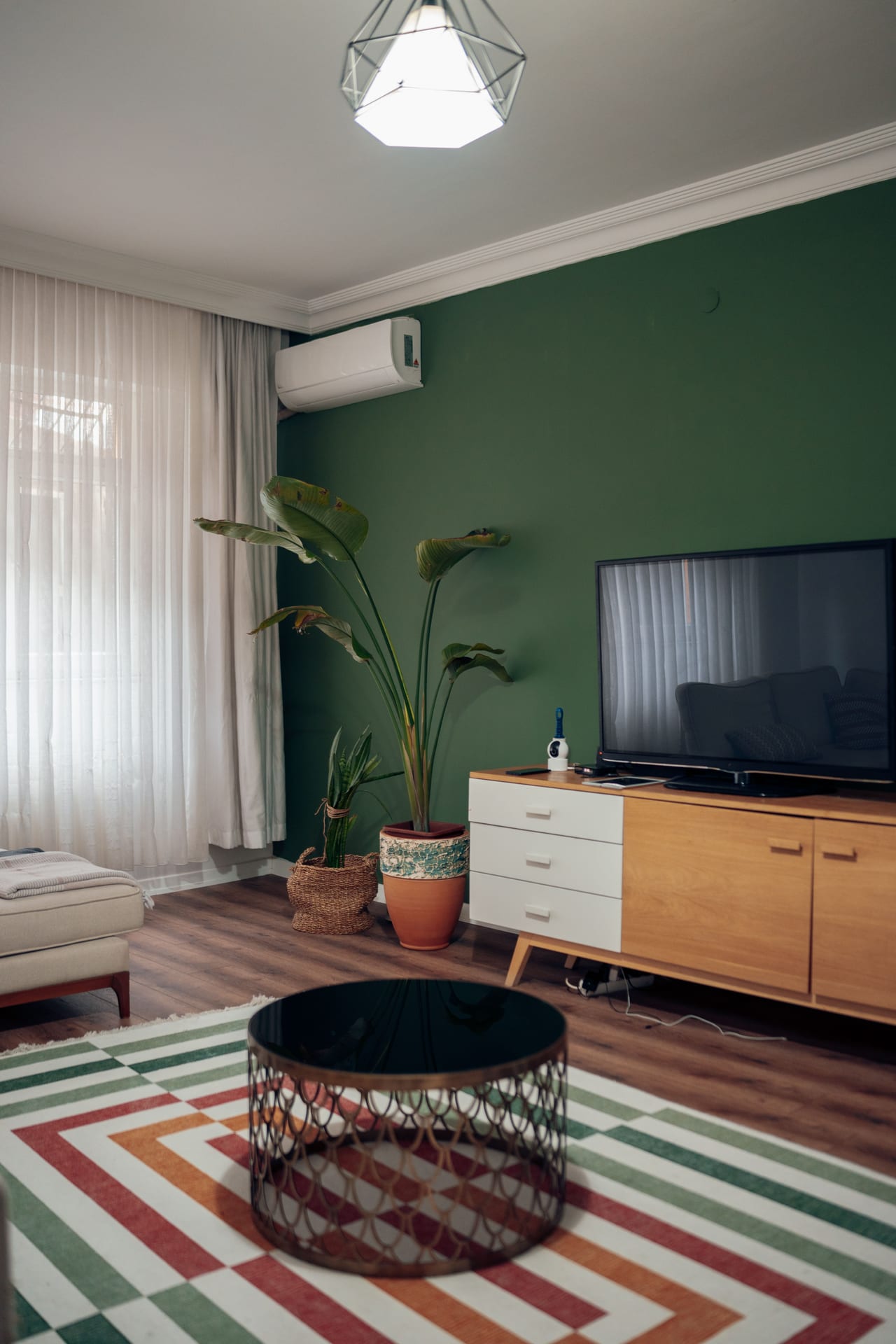 Projects Renovated living room with dark green accent wall, wooden TV unit and patterned rug in Alanya